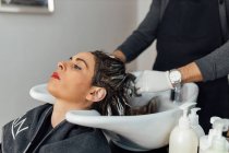 Cabeleireiro masculino corte no avental lavar o cabelo do cliente feminino na pia após o corte e tingimento no salão de beleza moderna — Fotografia de Stock