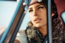Урожай модний жінка з квіткою на капелюсі в автомобілі, дивлячись далеко — стокове фото