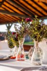 Primer plano de jarrones de vidrio transparente con racimos de flores frescas colocadas en la mesa para el evento - foto de stock