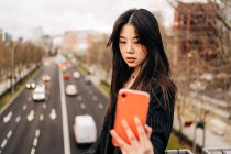 Cheveux longs brune asiatique femme en utilisant téléphone mobile dans la rue — Photo de stock