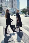 Vista laterale di bionda elegante giovani partner femminili in abbigliamento alla moda passeggiando su strada asfaltata in città — Foto stock