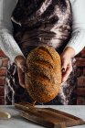 Crop boulanger femelle anonyme tenant du pain avec des graines de tournesol sur la table dans la boulangerie — Photo de stock