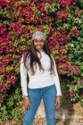 Femme afro-américaine déterminée aux cheveux longs et en tenue décontractée debout dans le parc par une journée ensoleillée et regardant la caméra — Photo de stock