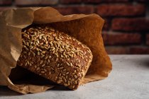 Pão inteiro saboroso com crosta marrom e sementes de girassol em cima na mesa à luz do dia — Fotografia de Stock