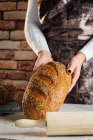 Crop anonymous female baker holding bread with sunflower seeds on table in bakehouse — Stock Photo