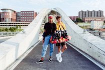 Dois adolescentes bonitos com skate em pé na ponte — Fotografia de Stock
