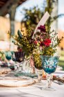 Close-up of served festive table with crystal glasses cutlery napkin on plate near bunch of fresh flowers for wedding — Stock Photo