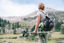 Atrás ver caminante femenina anónima en ropa casual con mochila con bastones nórdicos mientras está de pie en la colina pedregosa en el valle montañoso de Ruda en los Pirineos Catalanes - foto de stock