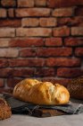 Pain blanc et seigle aux céréales et croûte appétissante sur planche à découper contre mur de briques en boulangerie — Photo de stock