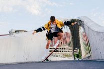 Adolescente caucasico che salta con uno skateboard nel bel mezzo del ponte in città — Foto stock