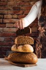 Анонимная женщина-пекарь урожая демонстрирует мягкий свежий хлеб с хрустящими семенами за столом в пекарне — стоковое фото