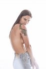 Side view of young female with bare breasts wearing casual jeans standing against gray background — Stock Photo