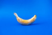 Вкусный спелый банан, покрытый прозрачной пластиковой пленкой, представляет собой концепцию промышленного сельского хозяйства на ярком фоне — стоковое фото