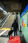 Hombre ciego caminando sobre escaleras mecánicas con perro guía - foto de stock