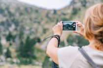 Voltar ver anônimo mochileiro feminino tirar fotos no smartphone de incríveis planaltos verdes pedregosos em Ruda Valley em Pirinéus catalães — Fotografia de Stock