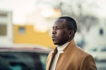 Вид сбоку на портрет уверенного молодого этнического мужчины в модном наряде, идущего по городской улице и смотрящего в солнечный день — стоковое фото