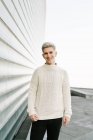 Side view of young stylish guy in trendy knitted sweater standing on city street near contemporary buildings on sunny day — Stock Photo