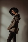 Side view low angle of determined female in trendy outfit standing in room near window and looking at camera — Stock Photo