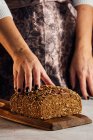 Crop padeiro fêmea anônimo segurando pão com sementes de girassol na mesa em padaria — Fotografia de Stock