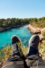 Schöne Aussicht auf Strand, Bucht mit türkisblauem Meerwasser, mit klarem Himmel, auf Klippen sitzend und den Füßen zuschauend, Insel Mallorca Spanien., — Stockfoto