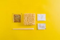 Layout von ungekochten Nudeln mit Gewürzzutaten und Sticks in Plastikverpackungen auf gelbem Hintergrund — Stockfoto