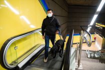 Hombre ciego caminando sobre escaleras mecánicas con perro guía - foto de stock