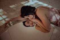 High angle of tender woman in nightgown lying with closed eyes on floor and reflecting in mirror — Stock Photo