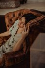 De cima de uma mulher tranquila sentada em cadeira de couro gasto e cabeça comovente enquanto relaxa em casa — Fotografia de Stock