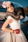 Full body of stylish female wearing long dress leather gloves and hat standing near vintage car against sea — Stock Photo