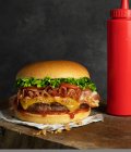 Detalhe de um delicioso hambúrguer com queijo e bacon na mesa de madeira — Fotografia de Stock