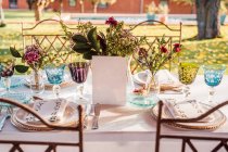 Alto ángulo de mesa festiva servida con vasos de cristal cubiertos servilleta en el plato cerca de ramo de flores frescas para la boda y la tarjeta de menú - foto de stock