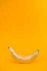 Вкусный спелый банан, покрытый прозрачной пластиковой пленкой, представляет собой концепцию промышленного сельского хозяйства на ярко-желтом фоне — стоковое фото