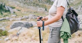 Caminhante fêmea anônima cultivada em roupas casuais com mochila com postes de passeio nórdicos enquanto estava em pé no topo de uma colina pedregosa no montanhoso Ruda Valley, em Pirinéus Catalães — Fotografia de Stock