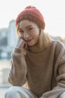 Content young female in knitted sweater and hat leaning on hand and looking at camera while sitting in city street — Stock Photo