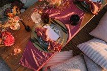 Вид зверху на дерев'яний стіл з конвертом і серветкою, розміщений на тарілці біля столових приборів і барвистих квітів на вулиці під сонячним світлом — стокове фото