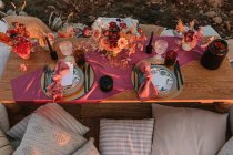 Сверху деревянный стол с столовыми приборами на тарелках подается на ткани возле красочных букетов цветов с винными бокалами во время свадебного торжества — стоковое фото
