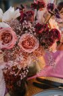 Rosas florecientes coloridas con pétalos tiernos colocados en jarrón en la mesa con plato y cubiertos durante la celebración de la boda en la calle - foto de stock