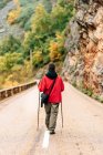 Back view female hiker in warm clothes with photo camera practicing Nordic walk in autumn forest and looking away dreamily — Stock Photo