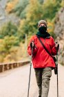 Female hiker in warm clothes with photo camera practicing Nordic walk in autumn forest and looking at camera dreamily — Stock Photo