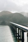 Мальовничі пейзажі дорожнього мосту над блакитною спокійною річкою, що тече через лісисті пагорби в туманний день — стокове фото