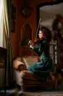 Повний вид на тіло досвідченої жінки-музикантки, яка грає на скрипці, сидячи на кріслі у старовинній кімнаті під час репетиції — стокове фото