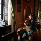 Vista lateral do músico feminino habilidoso tocando violino enquanto se senta na poltrona na sala de estilo vintage durante o ensaio — Fotografia de Stock