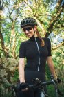 Happy female in sportswear with helmet standing with bicycle on nature — Stock Photo
