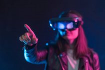Donna irriconoscibile con braccio teso con auricolare VR mentre esplora la realtà virtuale sotto la luce blu al neon — Foto stock