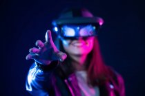 Femme méconnaissable avec un bras tendu portant un casque VR tout en explorant la réalité virtuelle sous la lumière bleue néon — Photo de stock