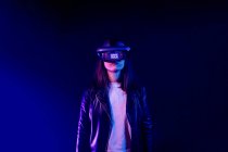 Unerkennbare Frau trägt modernes Headset mit Game Over-Aufschrift, während sie die virtuelle Realität im dunklen Raum mit Neonlicht in Wandnähe erkundet — Stockfoto