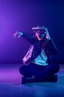 Неузнаваемая женщина с вытянутой рукой в VR гарнитуре, исследуя виртуальную реальность под синим неоновым светом возле стены с освещением проектора — стоковое фото
