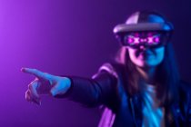 Unrecognizable female with outstretched arm wearing VR headset while exploring virtual reality under blue neon light — Stock Photo