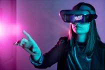 Mujer irreconocible con auriculares VR mientras explora la realidad virtual bajo la luz azul de neón - foto de stock