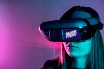 Donna irriconoscibile con auricolare VR mentre esplora la realtà virtuale sotto la luce blu al neon — Foto stock